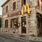 Façade d'un restaurant McDonald's en Corse avec architecture locale en pierre et végétation méditerranéenne en arrière-plan
